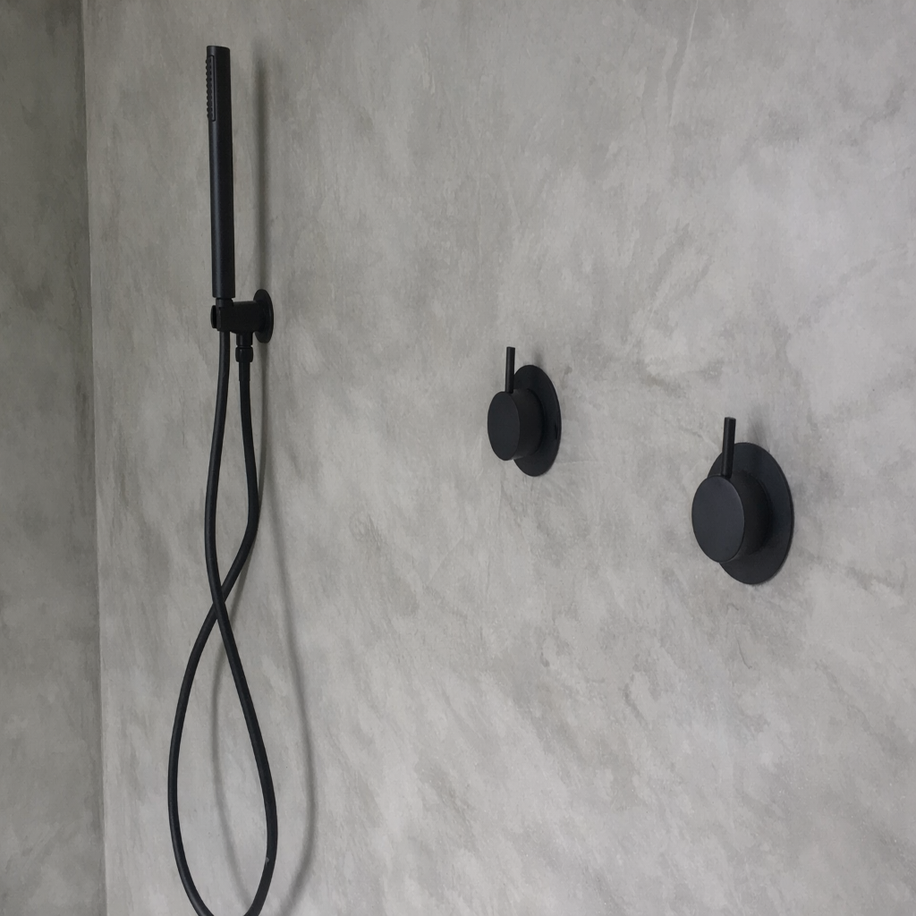Black shower head and control handles mounted on a concrete wall.