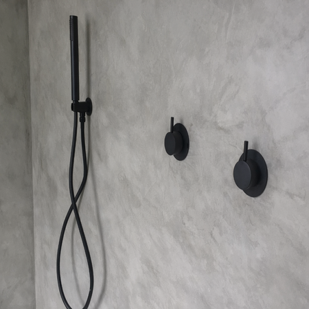Black shower head and control handles mounted on a concrete wall.