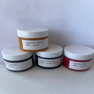 Four jars of different colored pigments stacked on a white surface with labels.