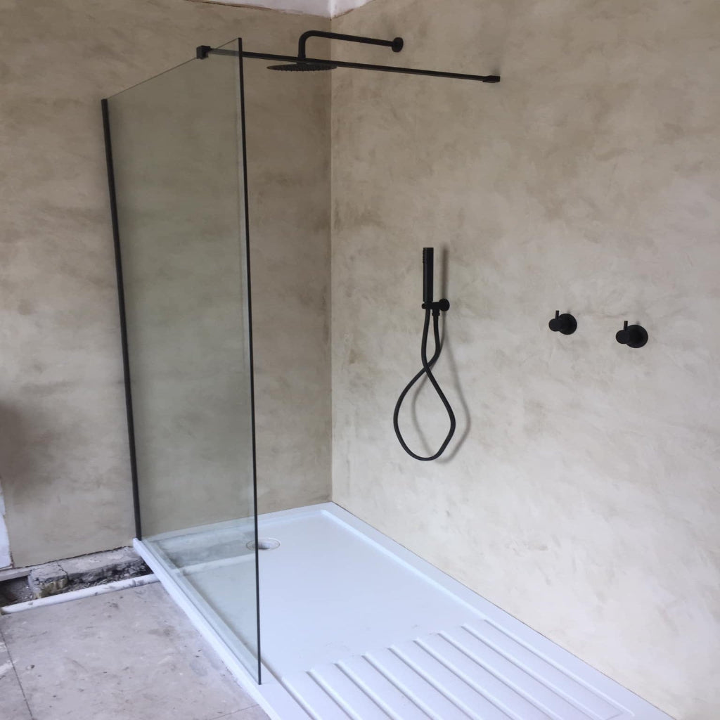 Modern shower setup with glass enclosure, shower head, and control handle on a concrete wall.
