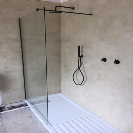 Modern shower setup with glass enclosure, shower head, and control handle on a concrete wall.